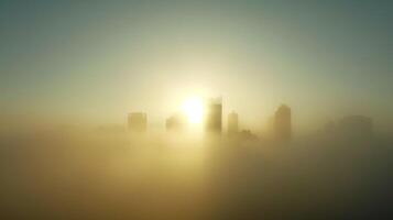 The hazy outline of a city skyline obscured by dense fog with the sun peeking through in the background photo