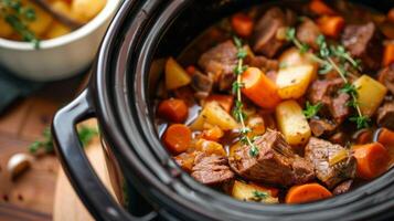A crockpot filled with savory beef stew with carrots potatoes and herbs visible photo