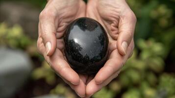 A pair of hands holding a smooth shiny black stone used for its healing properties in traditional medicine and showcasing the close relationship between minerals and healing photo