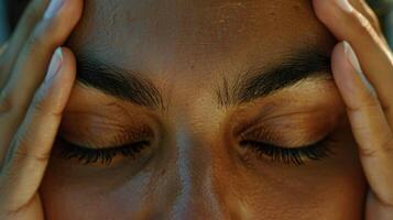 A closeup of a persons face eyes closed and relaxed with a faint smile while gently pressing their thumbs against their temples in a calming Ayurvedic selfmassage photo