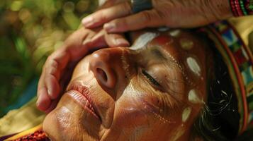 A shot of a participant receiving a healing touch from the shaman as they lay with eyes closed and a serene expression on their face. The shaman channels healing energy throug photo