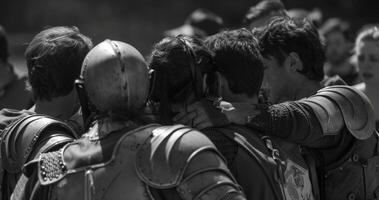 A group of jousting contestants huddle together backs towards the spectators as they strategize and discuss tactics for . photo
