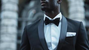 A dapper black man stands tall in a sharp tailored tuxedo with a crisp white dress shirt and bow tie. His suave look is completed with a shiny black patent leather shoe and a sleek photo