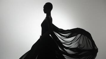 With a subtle curve of her hips and a tilt of her head a black model stands in a silhouette. The flowing fabric of her gown creates an alluring contrast against her smooth dark skin photo