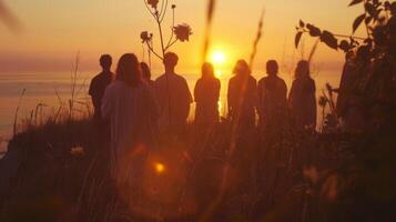 As the sun dips below the horizon a group of people stand in the fading light backs to the camera. They are participating in . photo