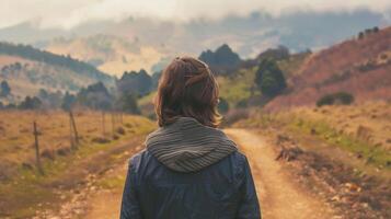 Walking along the winding dirt path a person gazes out towards the rolling hills in the distance. With back to the camera they . photo