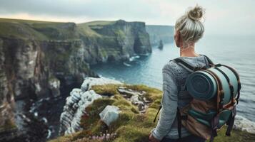 A middleaged woman takes a moment to pause and admire the beautiful view from a cliff yoga mat rolled up and slung over shoulder . photo