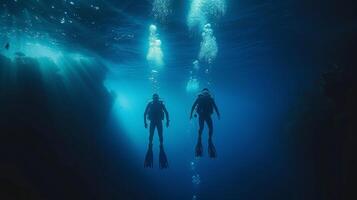Two scuba divers emerging from the deep blue backs to the camera as they ascend towards the surface dive lights creating . photo