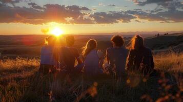 A group of friends sit on a grassy hill looking out at the last rays of the setting sun. They share a bittersweet moment reflecting . photo