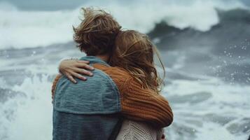 A couple embraces in a loving embrace backs turned towards the camera as they take in the calming sound of the waves crashing . photo
