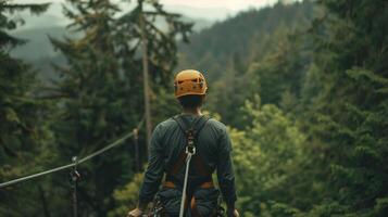 A man stands on top of a zip line platform back to the camera as prepares to soar through the forest canopy. wears a helmet . photo