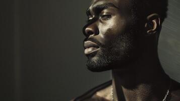 Against a backdrop of dark shadows a confident black man stands tall with his head held high. The interplay of light and shadows on his chiseled features highlights his refined sense photo