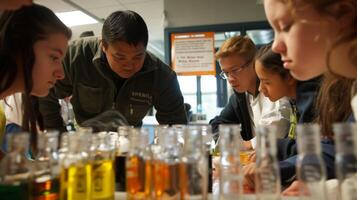 A group of students huddle around a biofuel kit in a school science lab taking notes and meticulously measuring ingredients. The teacher stands at the front of the room explaining photo
