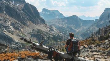 A hiker takes a rest on a fallen log leaning back against backpack as gazes out at the rocky terrain and rugged mountains in . photo