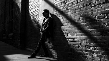 A black and white image of a photographer leaning against a brick wall lost in thought while waiting for their next subject to arrive. The shadows and angles in the composition add photo
