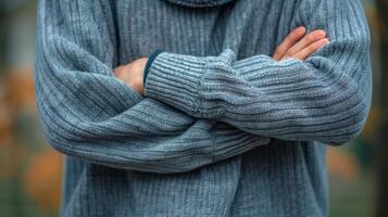 A person stands with their arms crossed over their stomach and their shoulders rounded forward giving off an air of insecurity and selfdoubt. photo