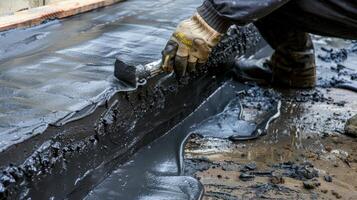 A closeup of a worker using a special tool to apply a layer of waterproofing tar to the corners and edges of a foundation ensuring complete protection photo