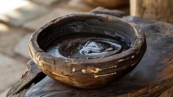 A handcarved wooden bowl is filled with a dark sticky paste. This mixture is made from various plants and minerals and is believed to have powerful healing properties whe photo