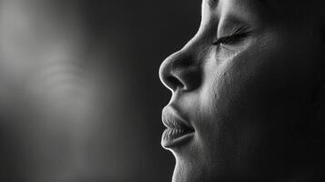 A black and white image of a persons face in profile their eyes closed and a peaceful expression on their face. Soft light illuminates their face creating a serene and introspectiv photo