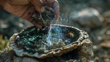 A hand pouring a small amount of smudging herbs into a traditional abalone shell ready to be lit and used for energy cleansing and purification photo