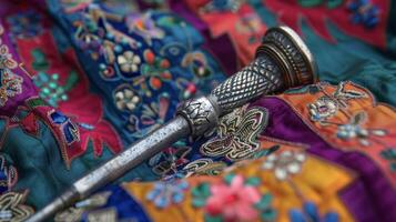 A small silver hammer with a precise needle attached at one end lies on top of a colorful embroidered cushion photo
