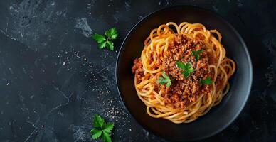 Overhead View of Spaghetti With Bolognese Sauce and Basil on a Black Plate photo