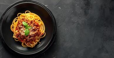 Overhead View of Spaghetti With Bolognese Sauce and Basil on a Black Plate photo