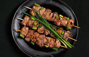 Grilled Beef Yakitori Skewers With Green Onions and Sesame Seeds on Black Plate photo