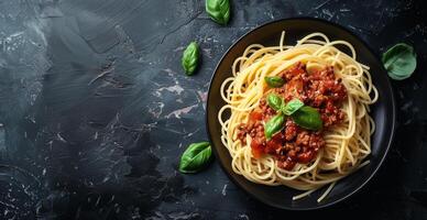Overhead View of Spaghetti With Bolognese Sauce and Basil on a Black Plate photo