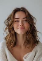 Woman With Short Brown Wavy Hair Smiling Against A White Wall photo