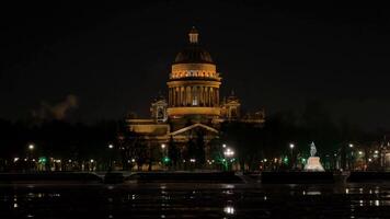 Nighttime view of Saint Isaacs Cathedral with illuminated facade and wet cobblestone foreground in Saint Petersburg, Russia, suitable for travel and history themes photo
