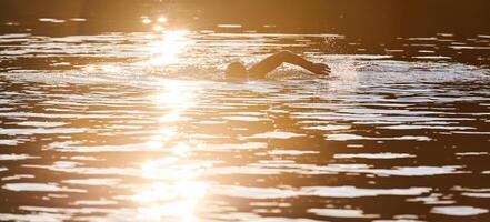 Triathlon athlete swimming on lake in sunrise wearing wetsuit photo