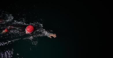 A determined professional triathlete undergoes rigorous night time training in cold waters, showcasing dedication and resilience in preparation for an upcoming triathlon swim competition photo