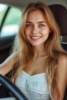 Woman with white top and red hair smiles while looking at the camera from behind the wheel of car photo