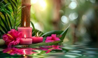 Three burning cosmetic pink candles on a bamboo stand, tropical flowers and leaves reflected in the water, sun bokeh, relaxation spa background photo