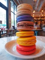 Colorful Macaron Tower on a Bright Day, A tower of brightly colored macarons stacked on a white plate, presented in a daylight-filled cafe atmosphere. photo