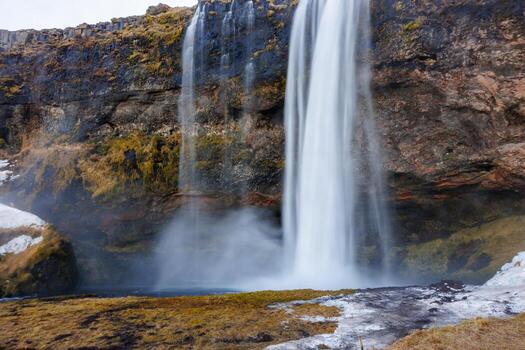 Seljalandsfoss cascade in icelandic setting runs off rocky hill with overflow of water. Magnificent panoramic view of river pouring down a slope in nordic scandinavian landscape. photo