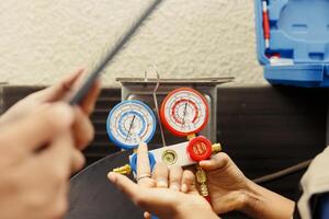 Close up of seasoned wireman holding pressure measurement device used for checking air conditioner refrigerant tank in need of repairing. Proficient expert using manometers to check freon levels photo