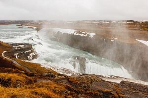 Gullfoss cascade in icelandic scenery, beautiful nordic landscape with snow and freezing cold water falling off cliff. River stream on top of frosty hill, scandinavian waterfall. photo