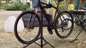 Modern bicycle is visible in the yard positioned on repair-stand for examining and mending. Outdoor various bike components await adjustments and restoration with professional work tools. photo