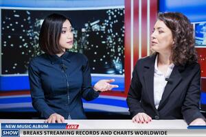 Journalists team talk about new music album, women night show hosts reveal song breaking top charts and records at global scale. Newscasters discuss about streaming and selling success. photo