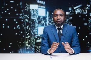 Anchorman working on live broadcast to discuss about latest events during night show segment, covering important topics. African american news reporter creating newscast with headlines. photo