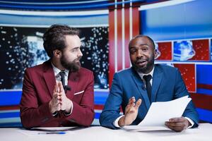 Reporters team presenting news segment in television studio to host late night show, addressing important global events. Diverse newscasters transmissing live reportage, international report. photo