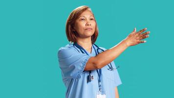 Close up shot of clinic worker doing swiping hand motion gestures, remotely controlling digital screen. Experienced nurse isolated over blue studio background working in high-tech modern hospital photo