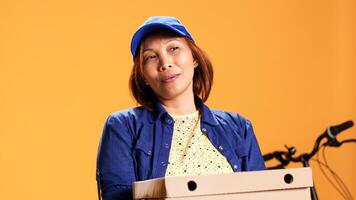 Hasty BIPOC employee waiting for client to answer door and pick up meal order. Portrait of bored courier isolated over studio background carrying stack of pizza boxes, close up photo