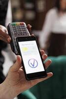 Detailed view of concierge helping elderly retired man with payment using cellphone and NFC technology. Close-up shot of male traveler paying using mobile device with assistance of hotel employee. photo
