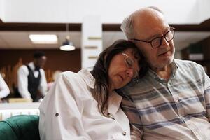 Two senior adults sleeping on cozy couch in a luxurious lounge area while waiting for check-in procedure. After long flight, caucasian elderly couple resting on comfortable sofa. Close up shot. photo