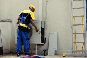 African american competent mechanic using dusting brush to clean dirty, clogged air filter restricting airflow, decreasing efficiency and reducing unit ability to cool air effectively photo