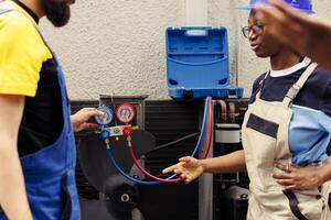 Licensed technicians team working with manifold gauges to check air conditioner refrigerant in need of maintenance. Qualified mechanics using barometer benchmarking hvac system component photo