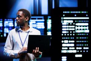 IT developer in server room using laptop to find firewall misconfigurations affecting mainframes performance and connectivity, leading to sluggish data transfer rates and poor client communication photo